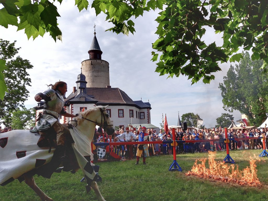 Ein Ritter zu Pferd reitet auf ein Feuer zu, im Hintergrund Publikum und die Burg Posterstein